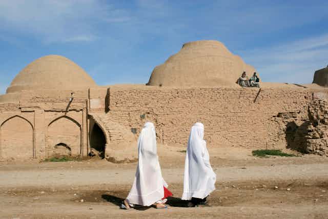 Two women in white burqas walking along a road.