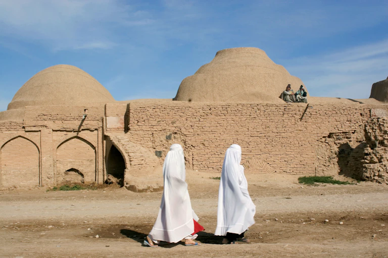 Two women in white burqas walking along a road.