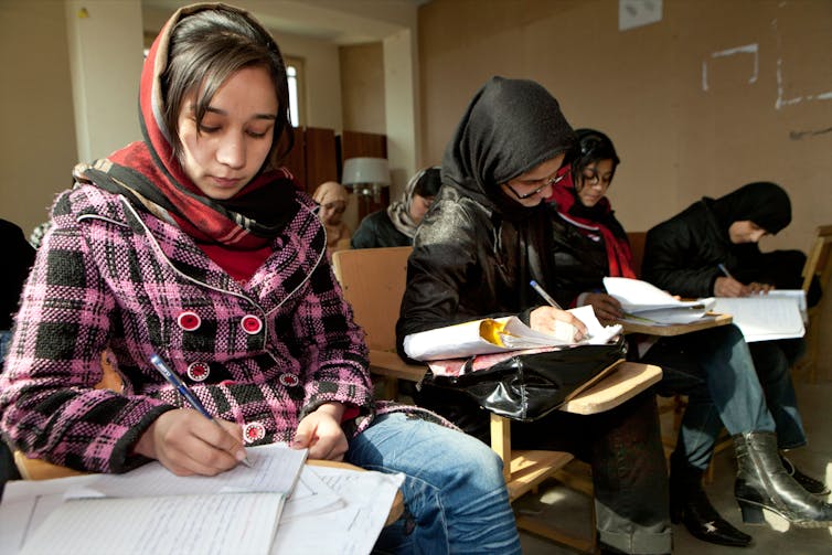 Girls writing down work in notebooks.