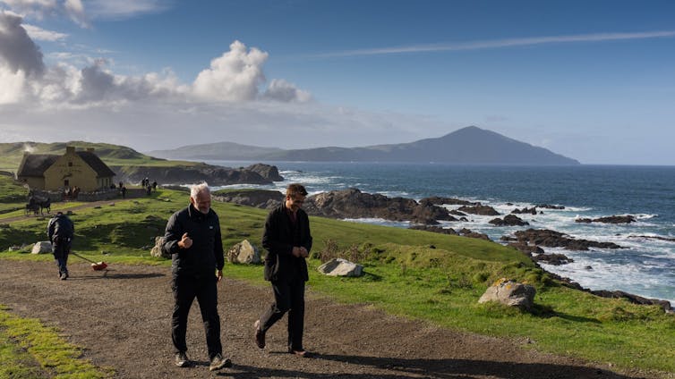 Martin McDonagh and Colin Farrell walk with a dramatic Irish seascape behind them.