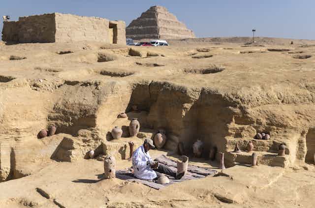 An archaeologist works at the site of the discoveries in Saqqara. A pyramid looms in the background