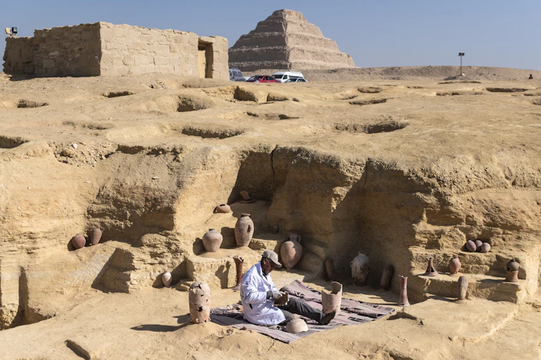 An archaeologist works at the site of the discoveries in Saqqara. A pyramid looms in the background
