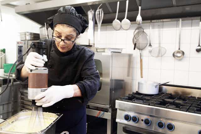 A woman in a black chef's hat and clothing mixing some batter in a restaurant kitchen.
