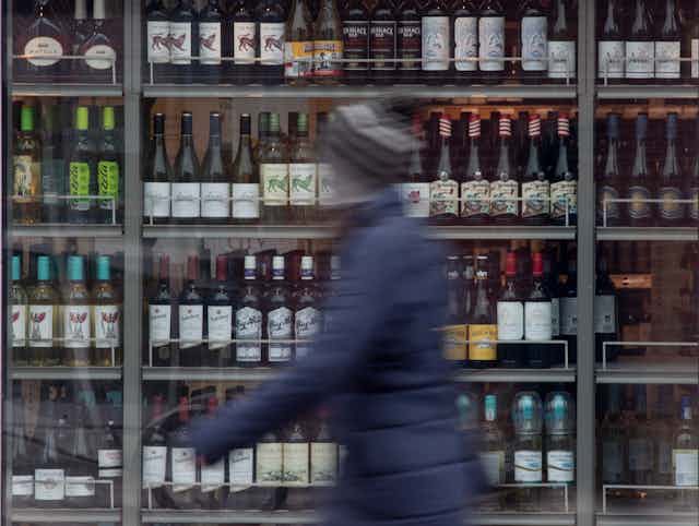 Blurred image of a person passing a display of wine on shelves