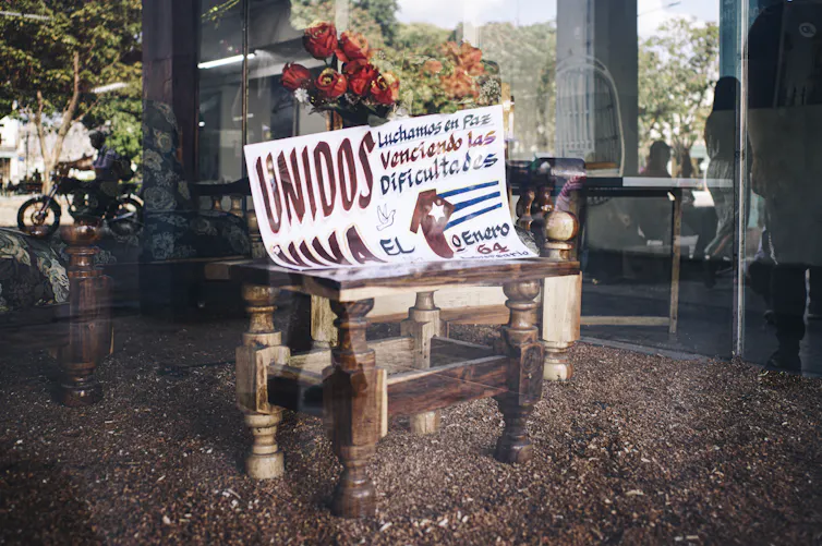 En el escaparate de una tienda que conmemora el 64 aniversario de la revolución cubana se puede leer: 'Unidos luchamos en paz, venciendo las dificultades'. - La Habana, Cuba, diciembre de 2022