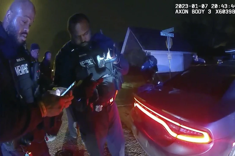 A video still shows two police officers in uniform stand next to a car.