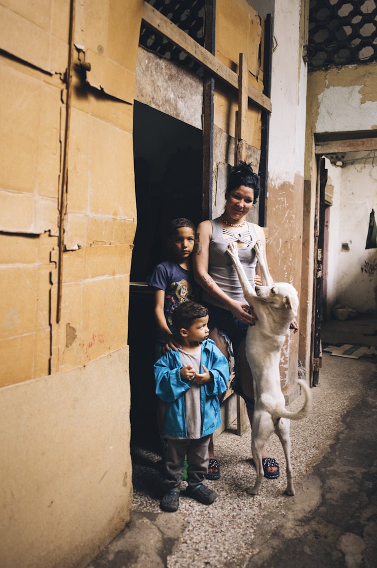 A woman and a dog pose for a portrait in the doorway of their living quarters in a Centro Habana _albergue_, Havana, Cuba, December 2022