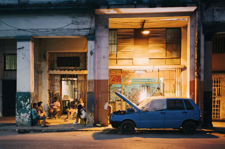 Una familia se relaja mientras un vecino repara su coche en La Habana, Cuba, diciembre de 2022.