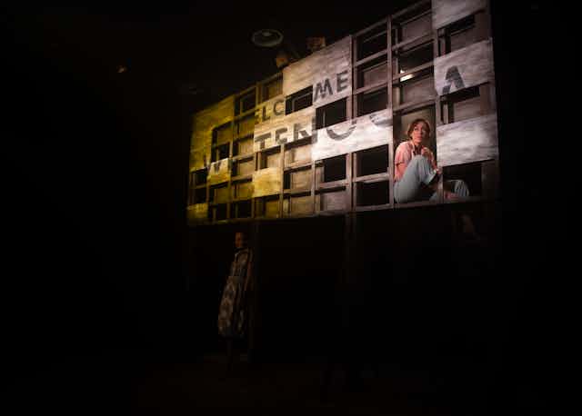 Production image: a woman sits in front of a broken sign.