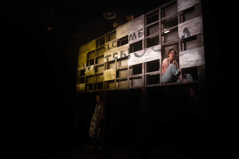 Production image: a woman sits in front of a broken sign.
