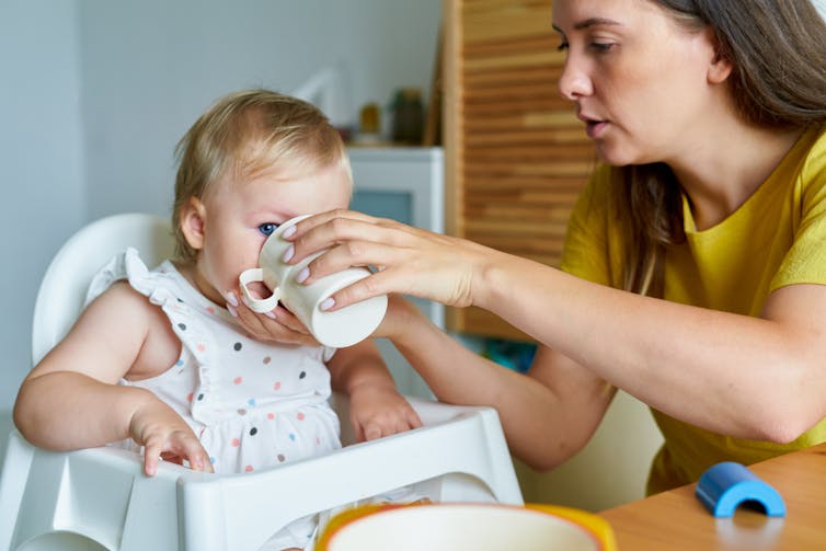 A mother helps a small child with a drink.