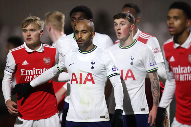 Football players on a field stand bunched together and staring ahead expectantly. They wear kit that is branded with Adidas and Nike logos and large words on their chest reading "Emirates, Fly Better" and "AIA".