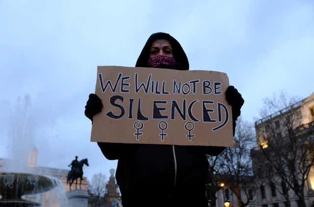 A protest on Trafalgar Square against police brutality and for women's rights holds up a cardboard sign saying we will not be silenced