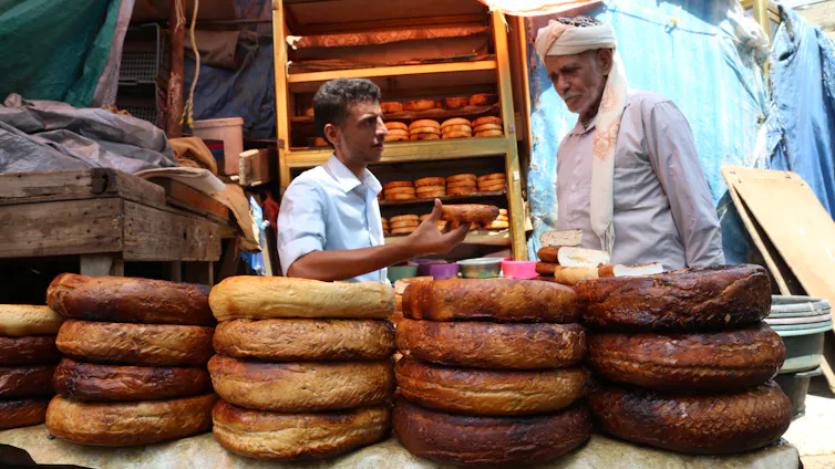 Two men behind large cheeses