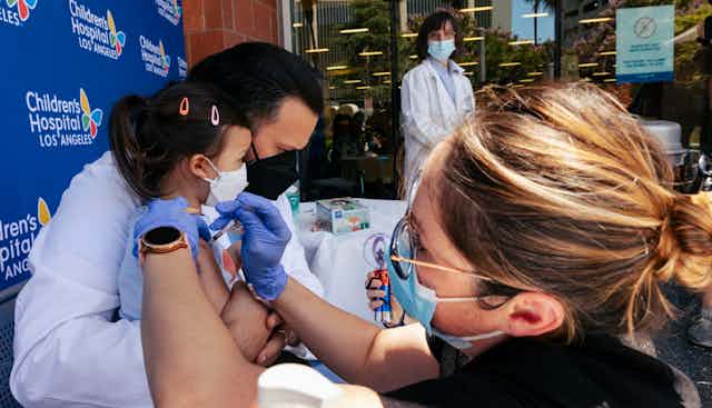 A woman wearing a mask and gloves gives a baby a shot
