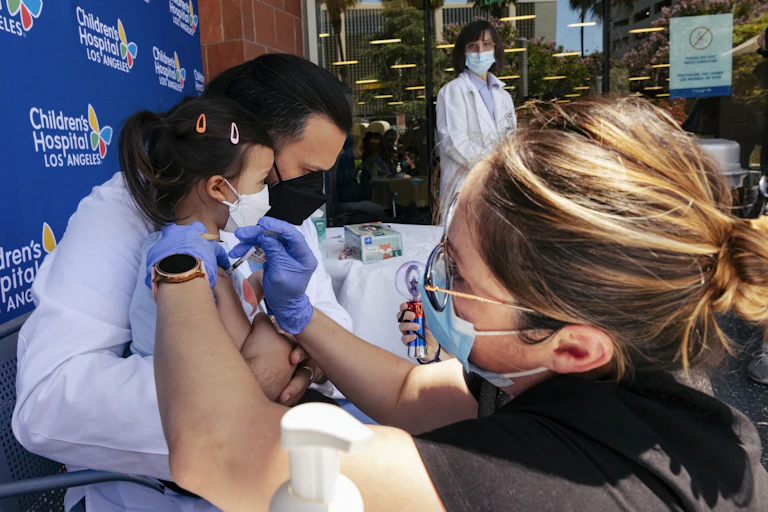 A woman wearing a mask and gloves gives a baby a shot
