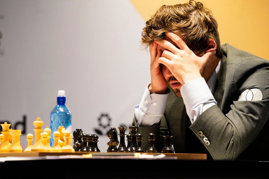 A man holds his head in his hands as he ponders a chess move.