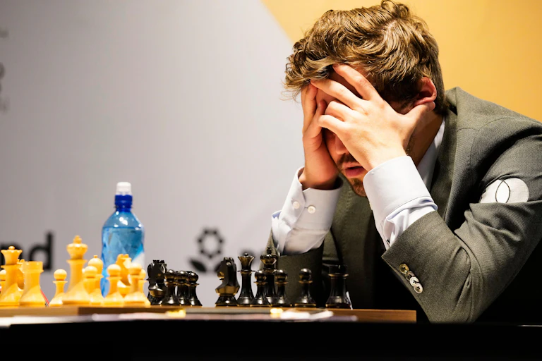 A man holds his head in his hands as he ponders a chess move.