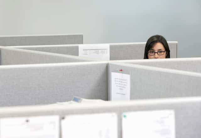 woman peeks out over cubicles