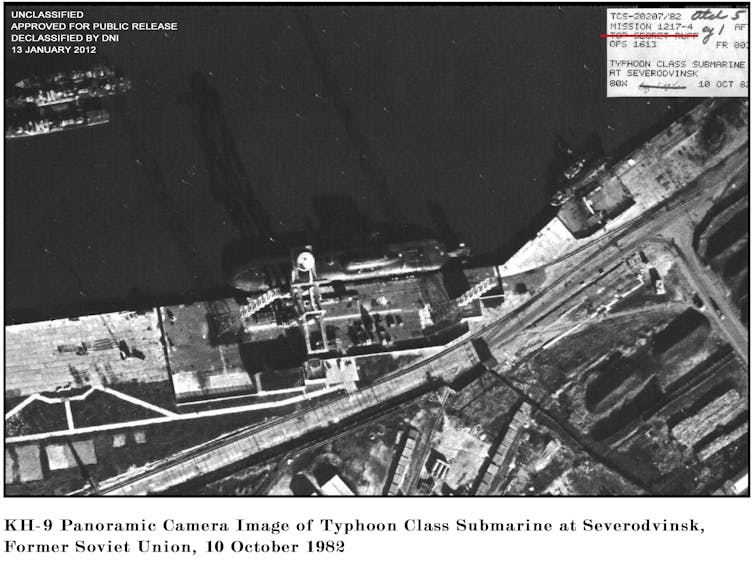 a black-and-white view from high above a seaport showing a submarine