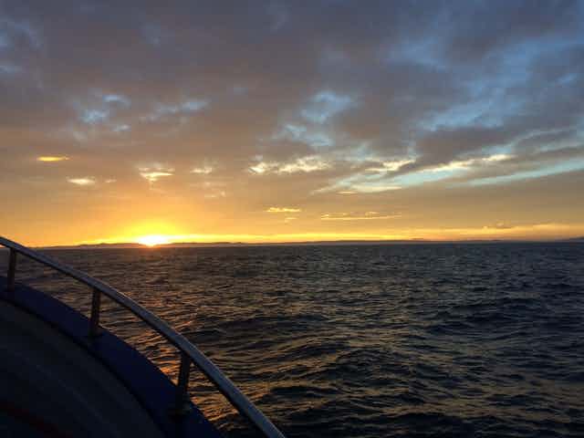 The sun sets over the ocean, viewed from a boat at sea