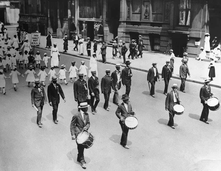 A group of black men, women and children are marching on a street.