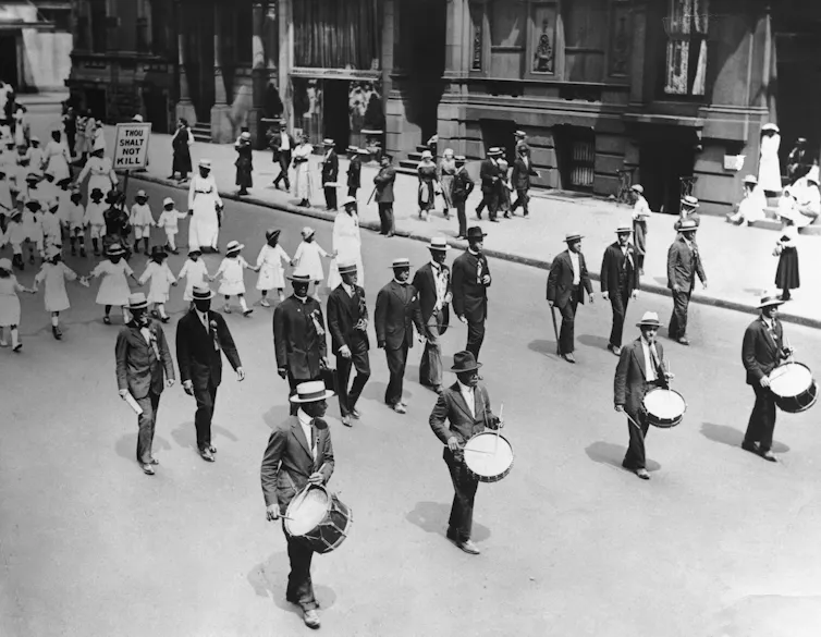A group of black men, women and children are marching on a street.