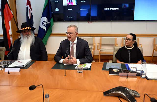 Prime Minister Anthony Albanese sits with Patrick Dodson and Linda Burney in what looks like a conference setting.