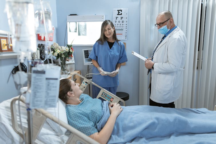 Une patiente, sur son lit d’hôpital, est entourée d’une infirmière et d’un médecin