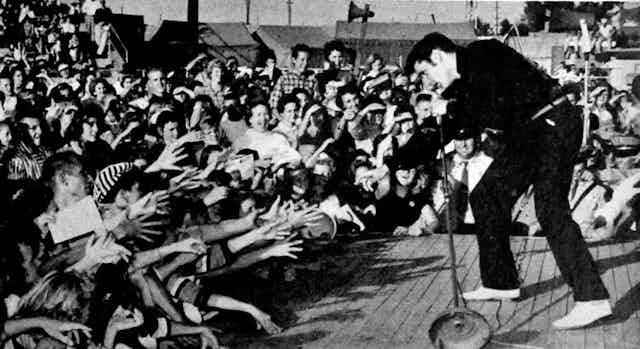 Elvis canta frente a un montón de fans que alargan los brazos para tocarle.