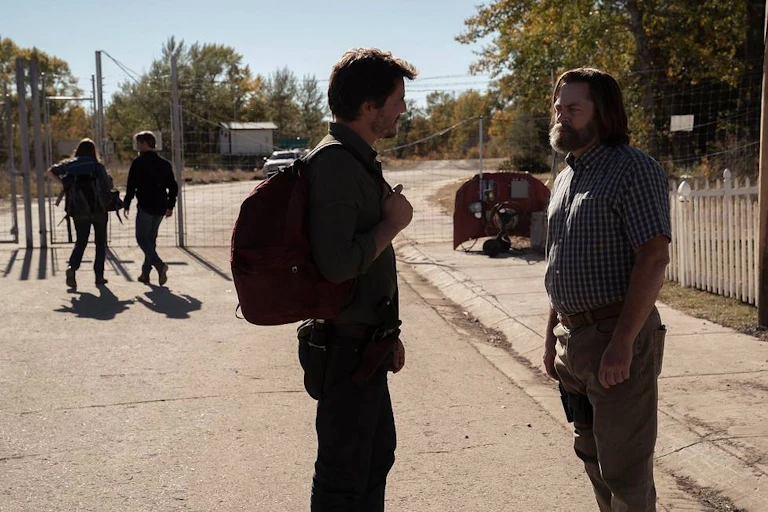Photo of two men talking, two people in background going through chain link fence