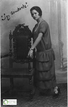 Retrato de una mujer a principios de siglo XX que está de pie y lleva un vestido largo.