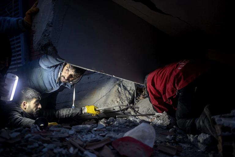 People search through rubble by torchlight.