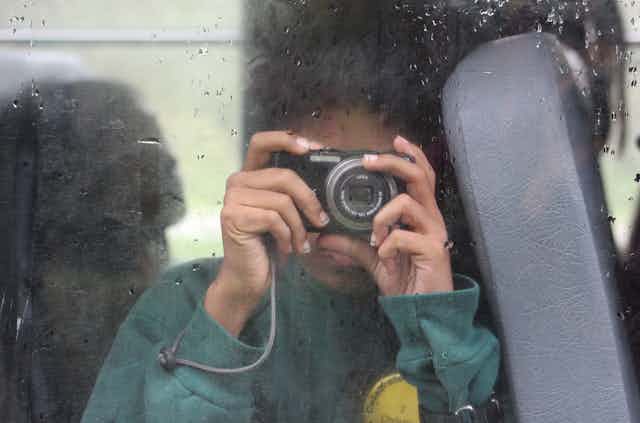 A student on a school bus holding a digital point-and-shoot camera.