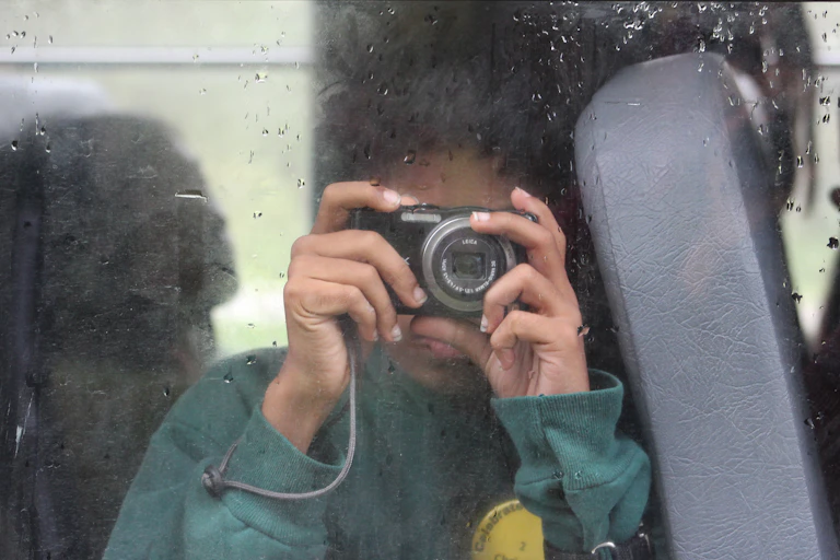 A student on a school bus holding a digital point-and-shoot camera.