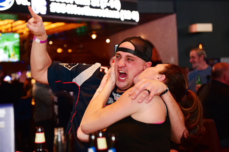 Excited man in football jersey and backwards hat being kissed by a woman on the cheek.