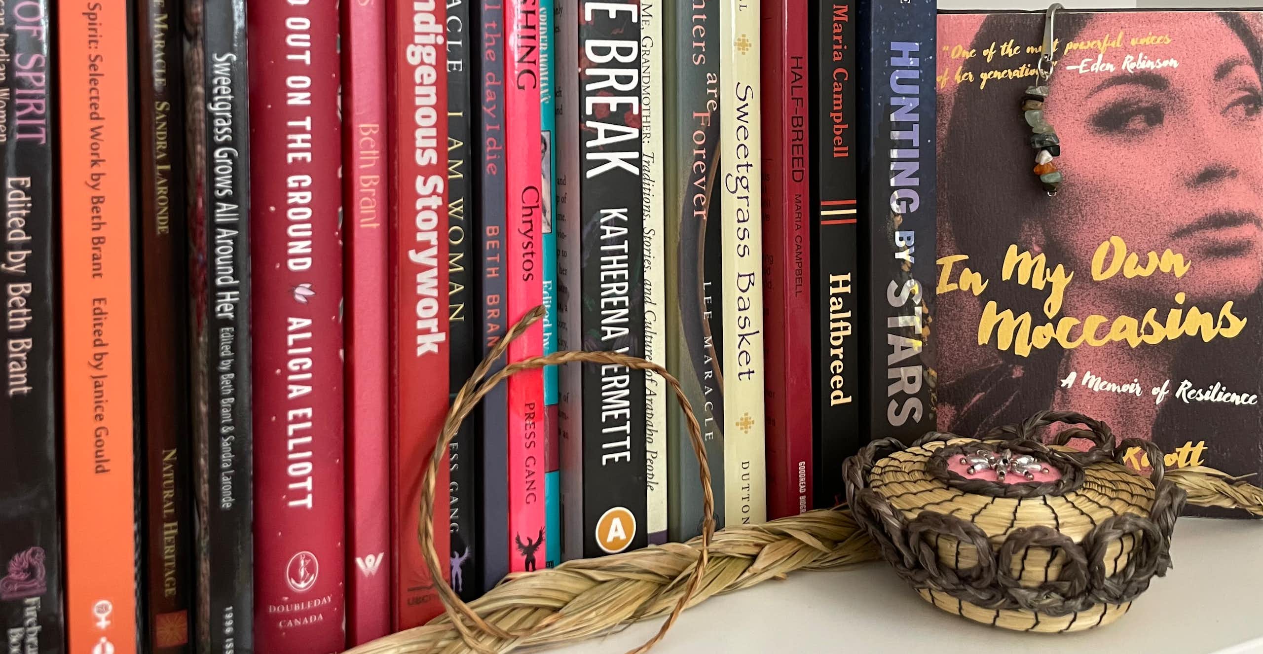 A row of books seen with a braid of sweetgrass in front.