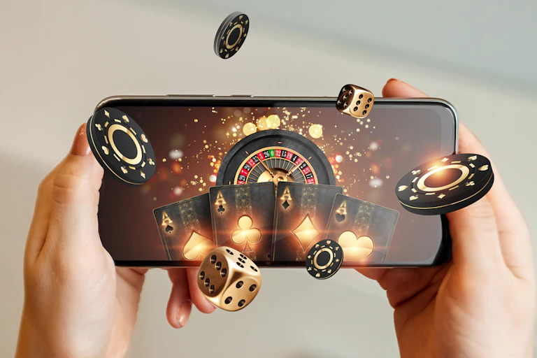 online casino, in a man's hand a smartphone with playing cards, roulette and chips, black-gold background. Internet gambling