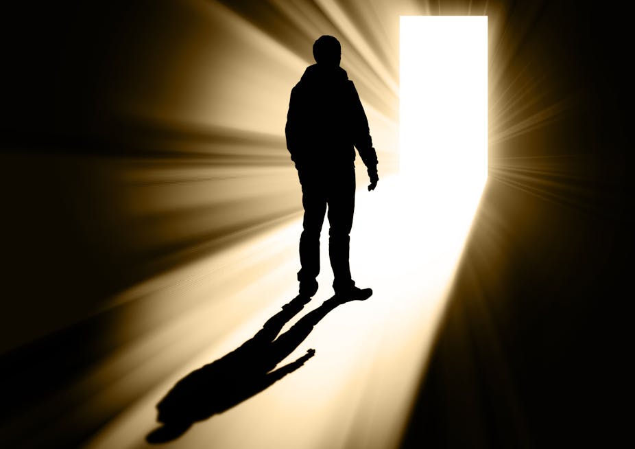 Silhouette of man walking toward bright doorway.