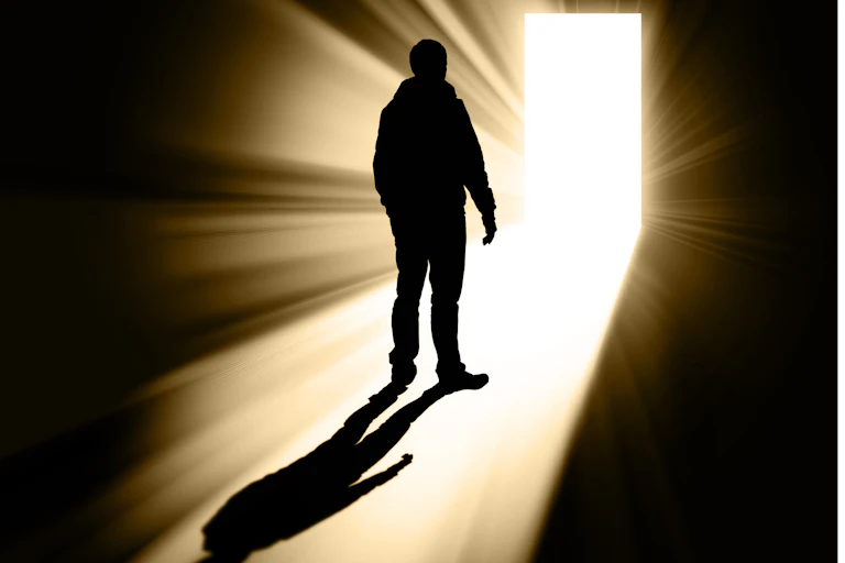 Silhouette of man walking toward bright doorway.