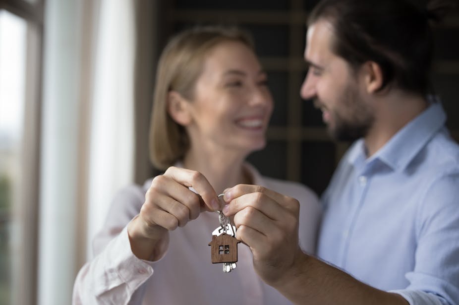 A man and a woman smile at each other. They have their arms out and are holding a set of keys.