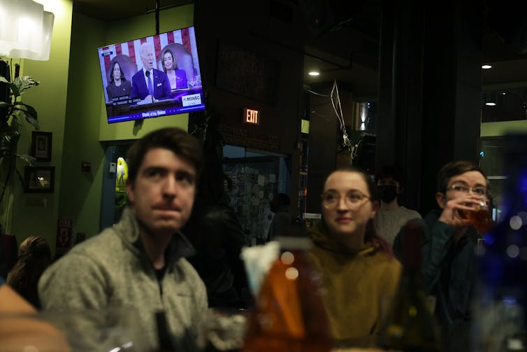 Two women and a man at a restaurant watch a screen showing US President Joe Biden.