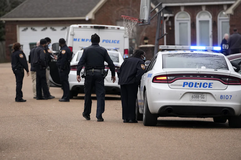 Police officers in uniform stand by police vehicles.