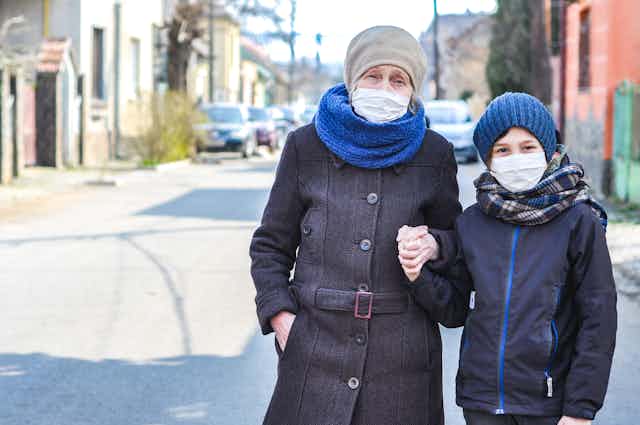 An elderly woman and young boy holding hands and wearing face masks.