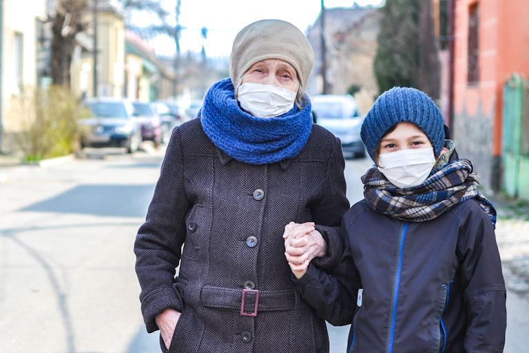 An elderly woman and young boy holding hands and wearing face masks.