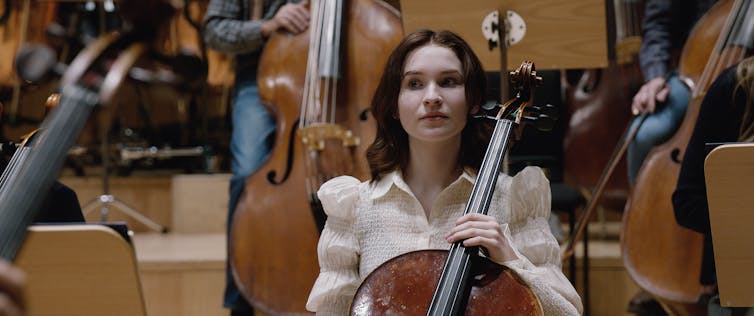 a woman sits and looks to be playing the cello