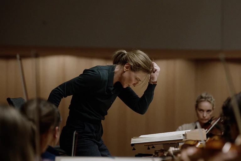 a white woman, standing, head down, fist in the air, conducts an orchestra