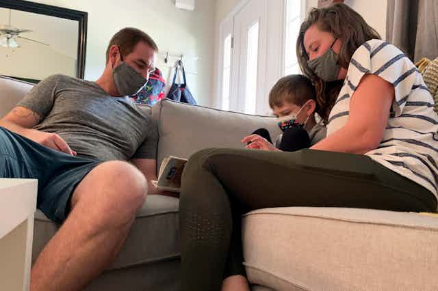 Two adults sit on a couch with a child between them, holding a book.
