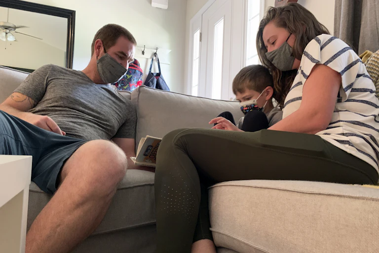 Two adults sit on a couch with a child between them, holding a book.