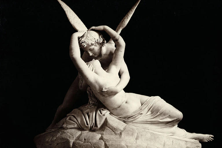 A white statue of a winged man embracing a woman draped in a cloth.